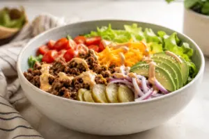 Burger bowl with seasoned ground beef, lettuce, tomatoes, pickles, cheddar cheese, and creamy sauce