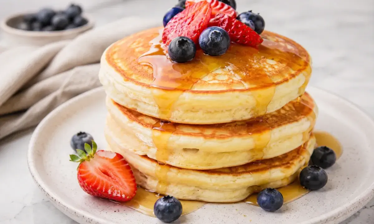 A stack of fluffy pancakes topped with syrup, strawberries, and blueberries